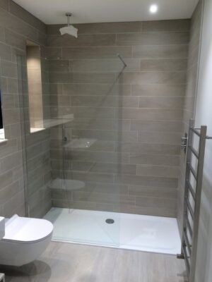 Modern grey scale bathroom with large walk in shower, toilet and sink. Tiled from floor to ceiling, read our privacy policy for more details if needed.