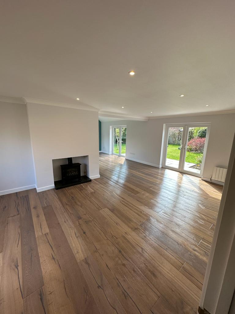 A beautiful open plan living room with wooden floor and ceiling spot lights.